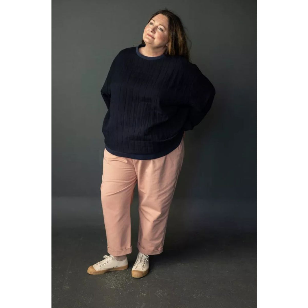 Person wearing a navy sweater and pink pants against a dark background