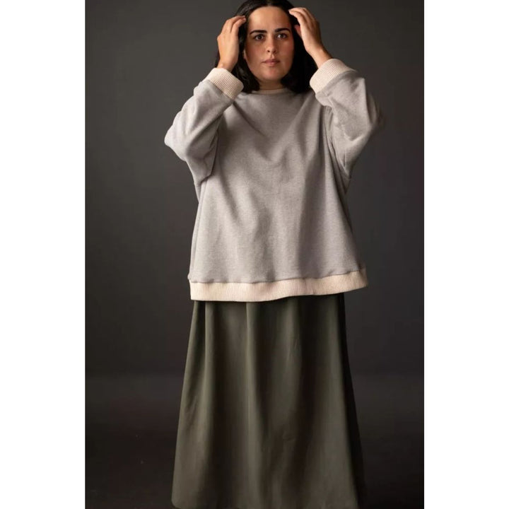 Woman wearing a light gray sweater and dark green skirt against a dark background