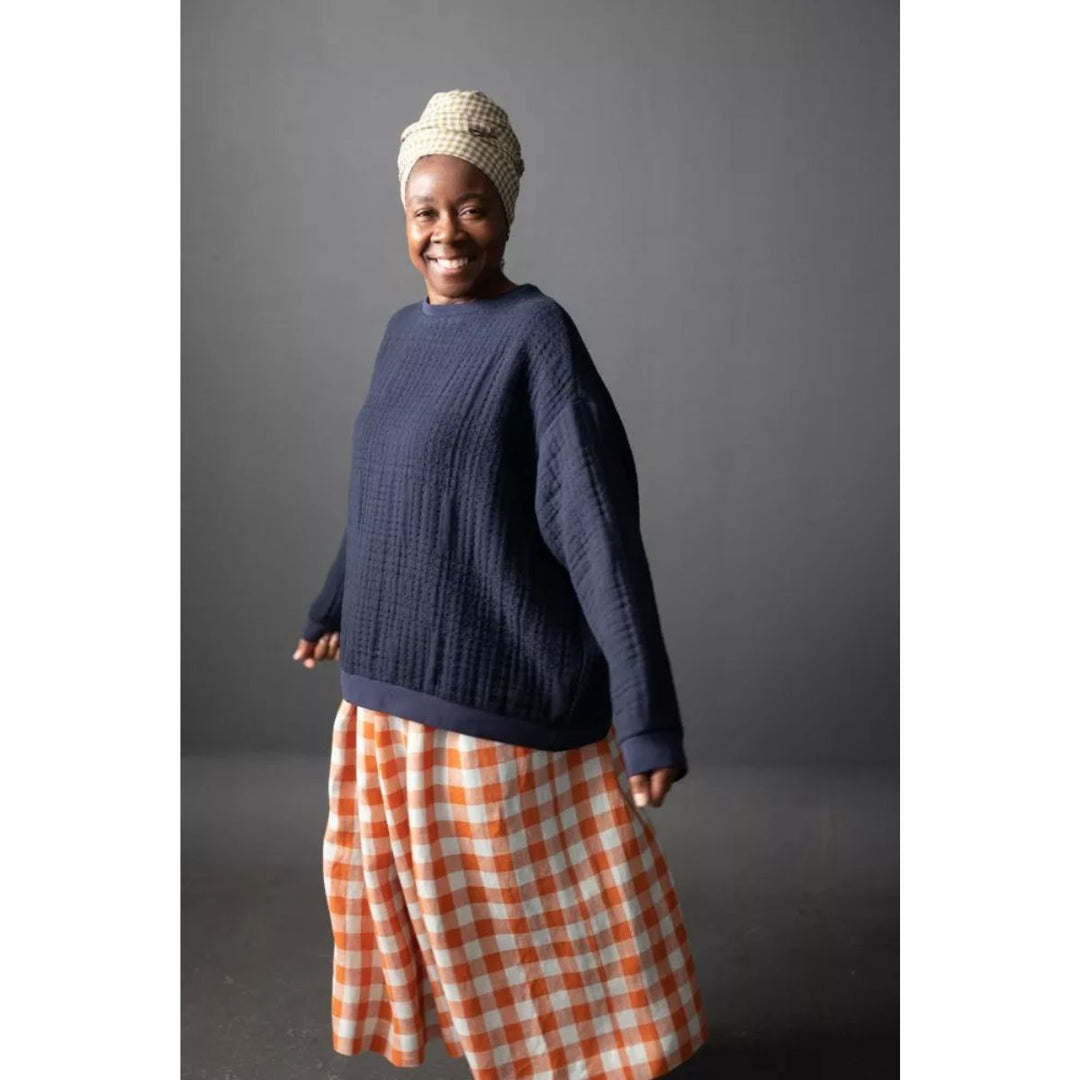 Person wearing a navy sweater and orange checkered skirt against a gray background