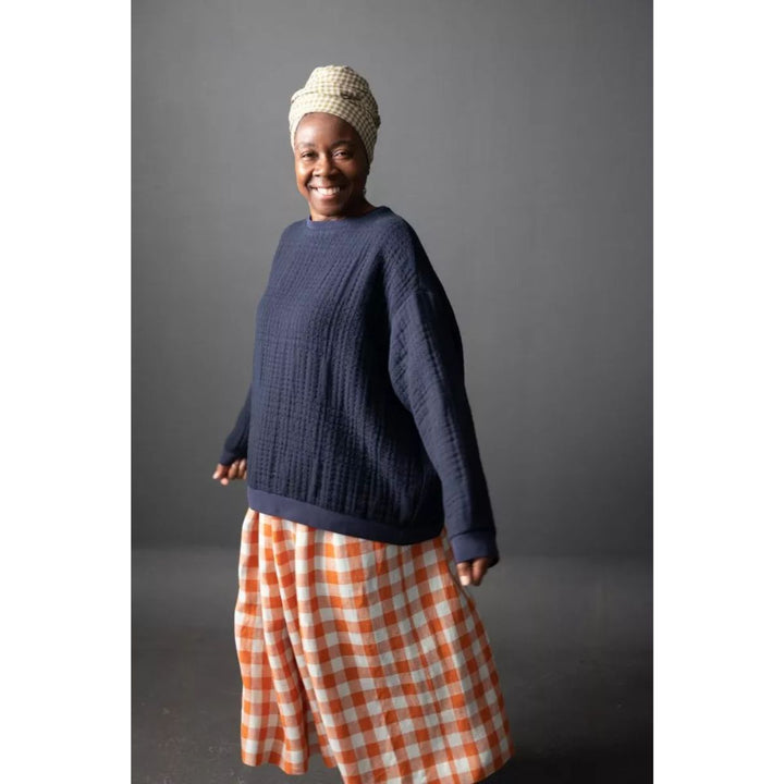 Person wearing a navy sweater and orange checkered skirt against a gray background