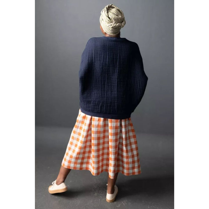 Person wearing a navy sweater and orange checkered skirt with a gray background