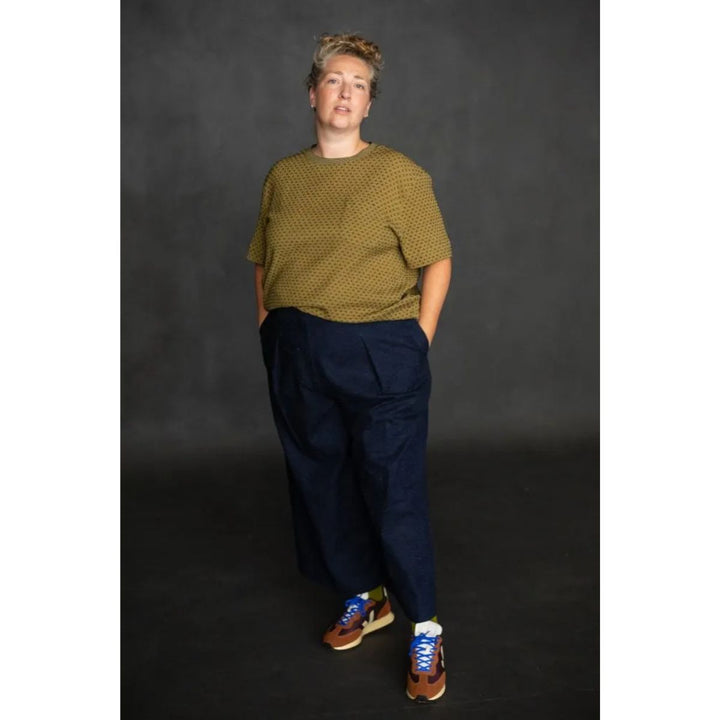 Person wearing a green patterned sweater and navy pants against a dark background