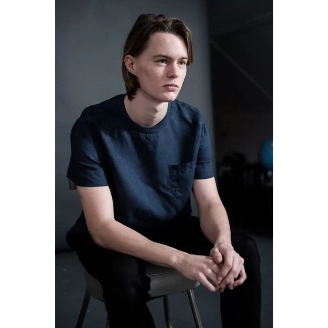 Person wearing a dark blue t-shirt sitting on a chair against a dark background