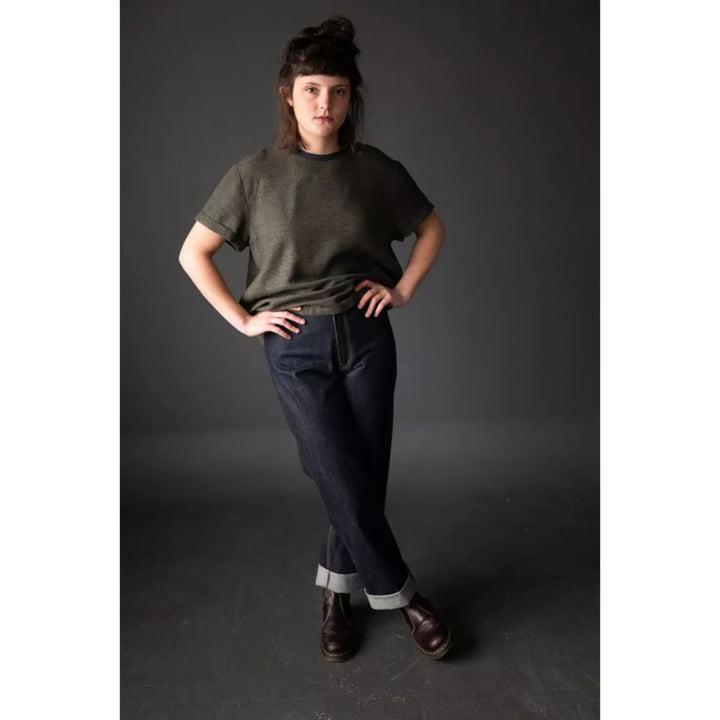 Person wearing a green t-shirt and dark jeans against a gray background