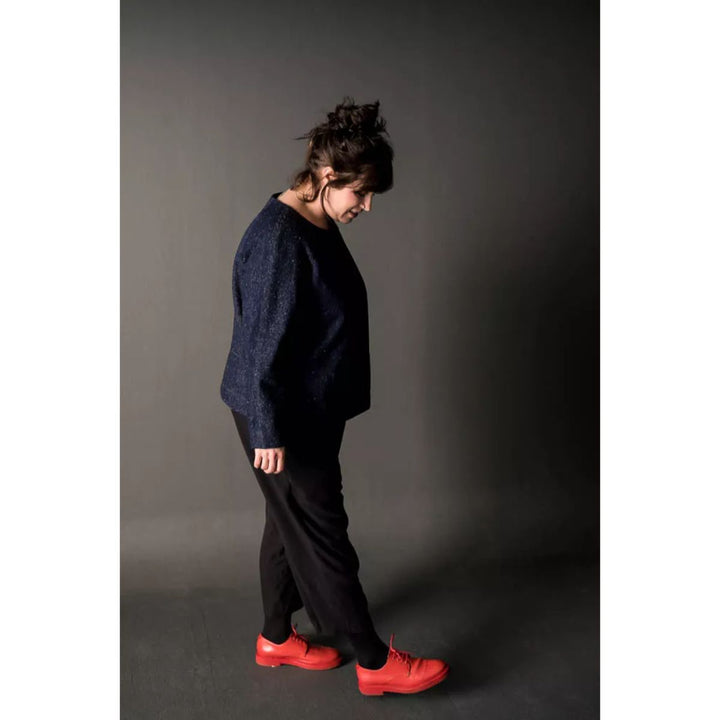 Person wearing a dark outfit with red shoes on a gray background