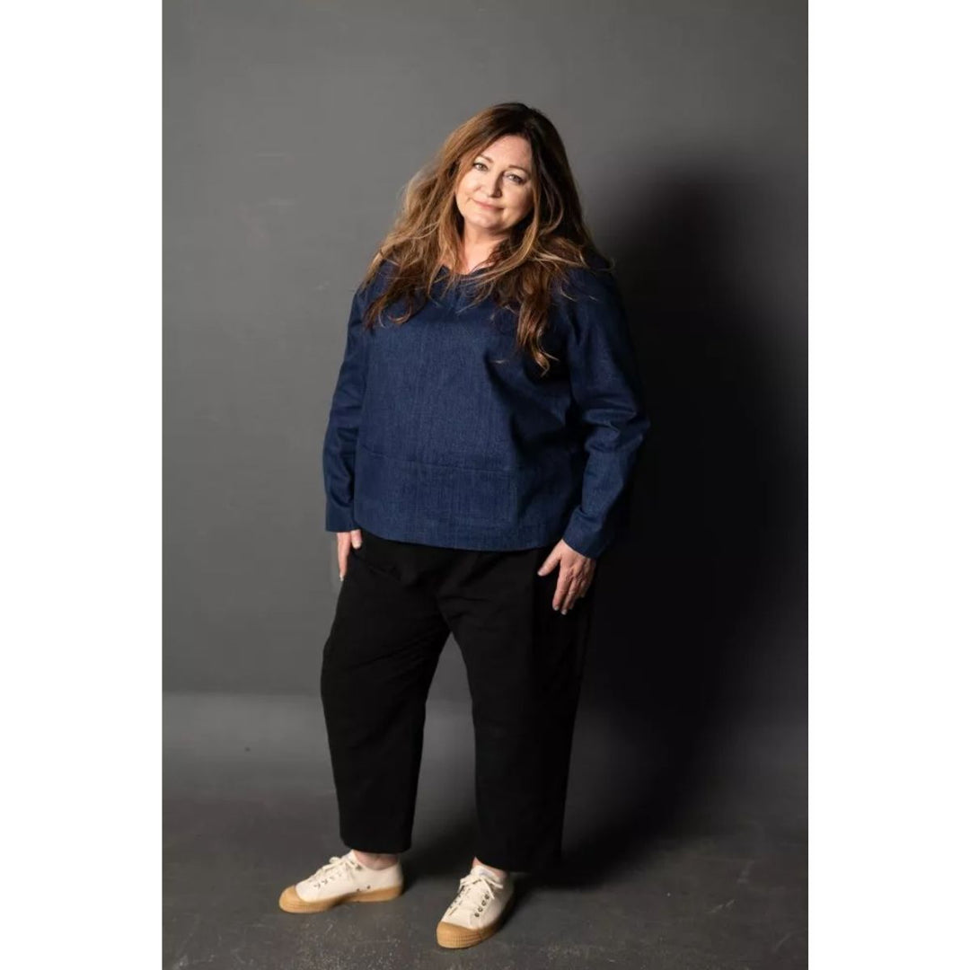 Woman wearing a blue sweater and black pants against a gray background