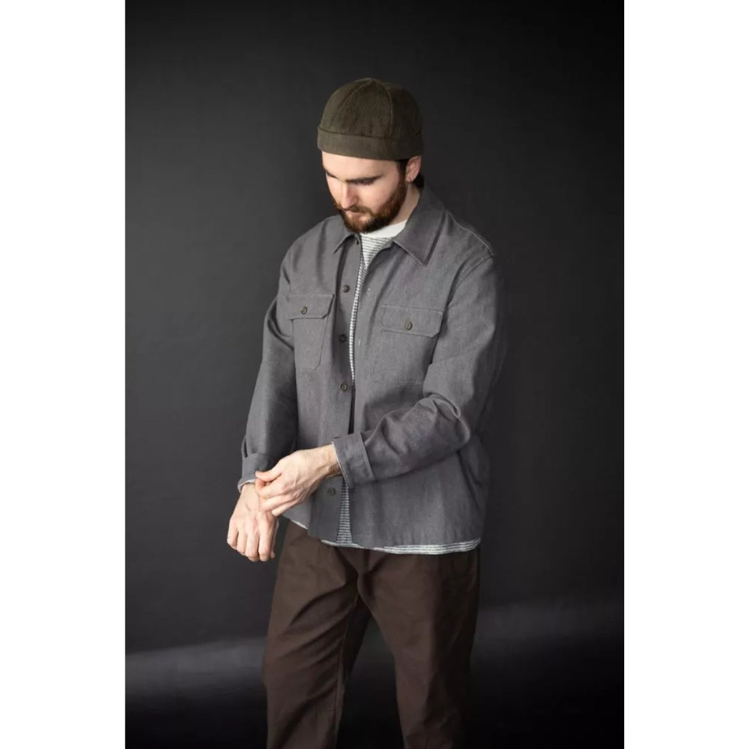 Man wearing a gray jacket and brown pants against a dark background