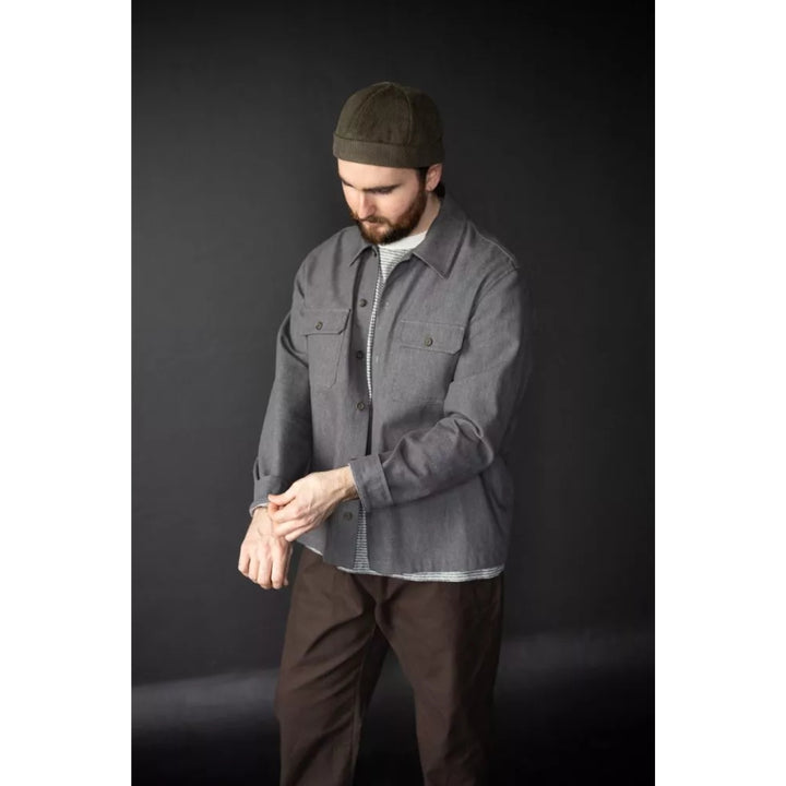 Man wearing a gray jacket and brown pants against a dark background
