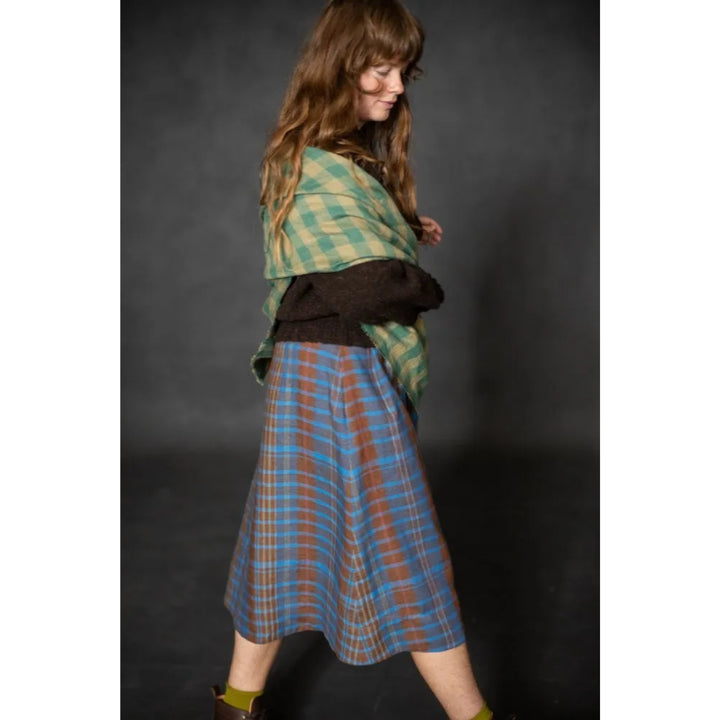 Woman wearing a green plaid shawl and blue plaid skirt against a dark background