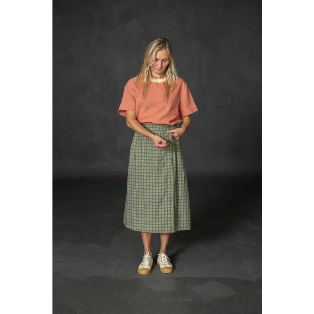 Woman wearing a pink shirt and green plaid skirt on a dark background