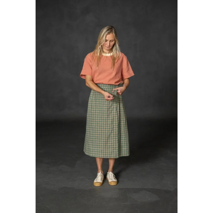 Woman wearing a pink shirt and green plaid skirt on a dark background
