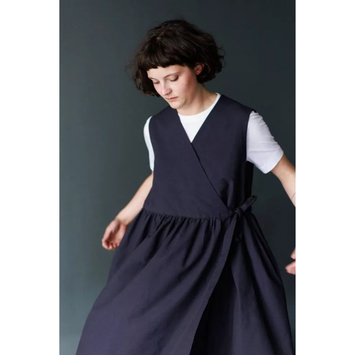 A model wearing a dark navy wrap-style dress over a white short-sleeve t-shirt, captured in a moody studio setting with a dark gray background.