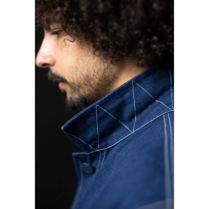 Close-up side profile of a man wearing a dark blue denim jacket with white contrast stitching on the collar, set against a solid black background.