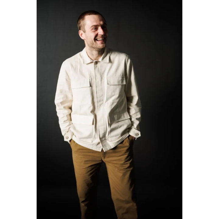 Man wearing a light-colored shirt and brown pants against a dark background