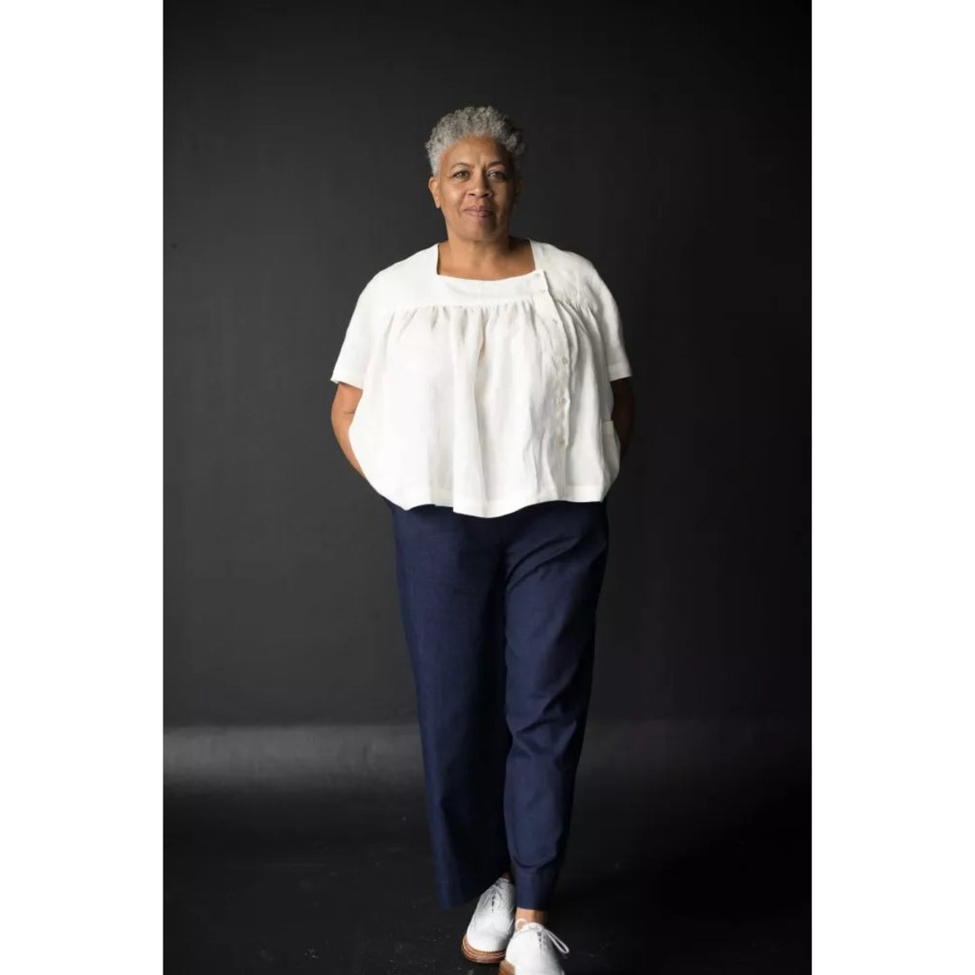Person wearing a white blouse and navy pants against a black background