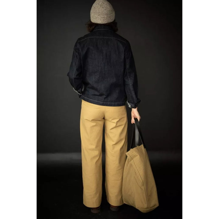 Person wearing a dark jacket and beige pants holding a bag against a black background