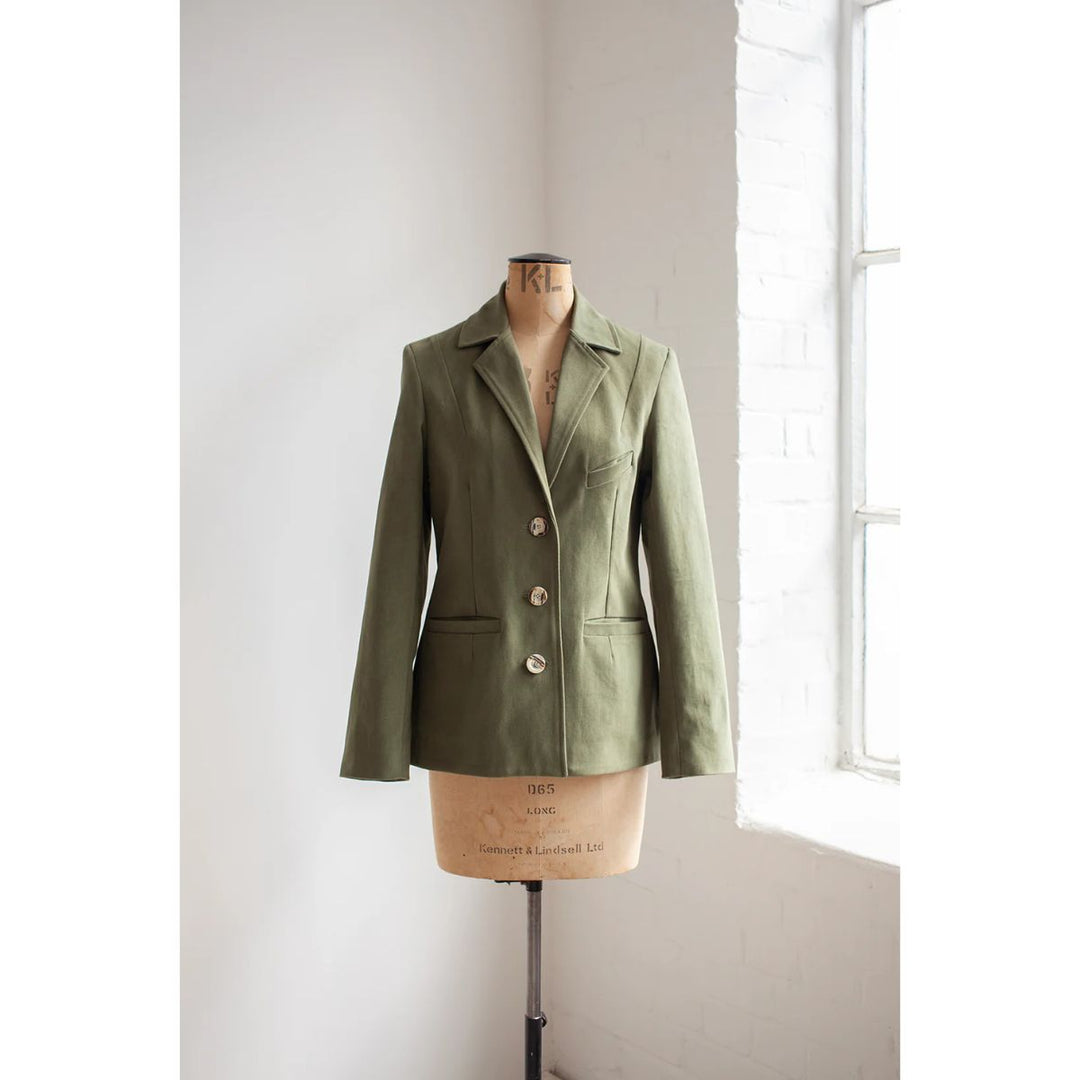 Green blazer on a mannequin against a white wall with natural light.