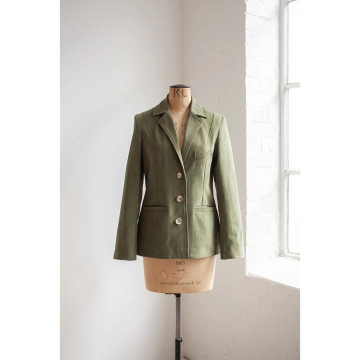 Green blazer on a mannequin against a white wall with natural light.