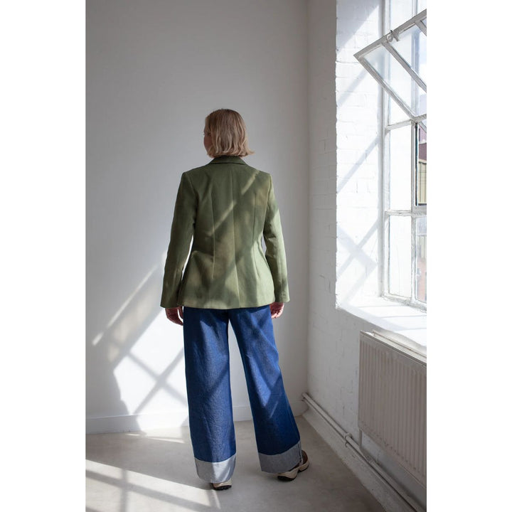 Person wearing a green jacket and blue pants standing in a room with sunlight streaming through a window.