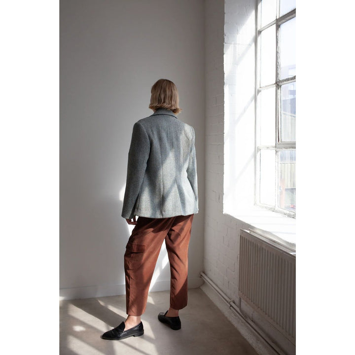 Person wearing a light blue jacket and brown pants standing in a room with a large window.