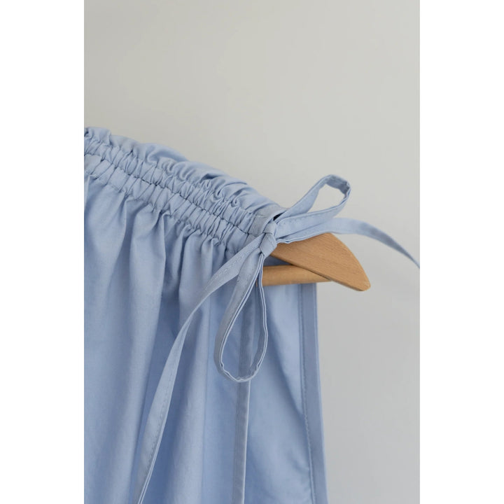 Close-up of a light blue gathered fabric item, likely a skirt or drape, hanging from a wooden hanger against a plain light gray background.