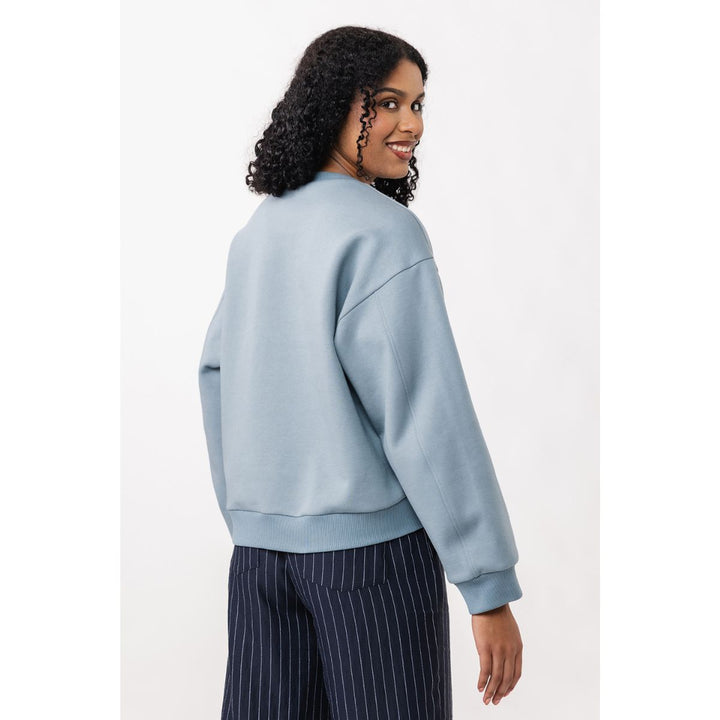 Woman wearing a light blue sweatshirt and dark pinstripe pants on a white background