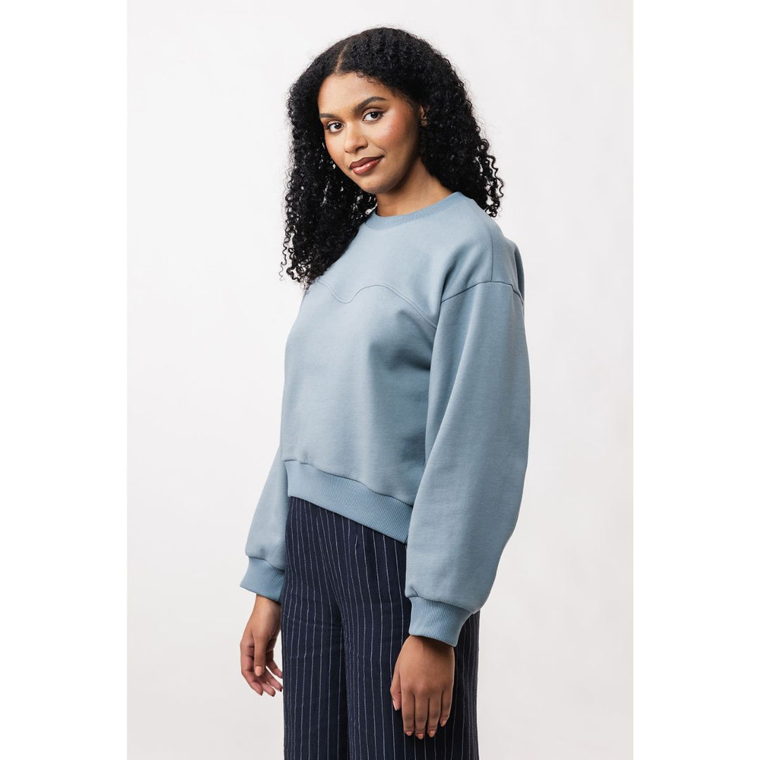 Woman wearing a light blue sweatshirt and dark pants on a white background