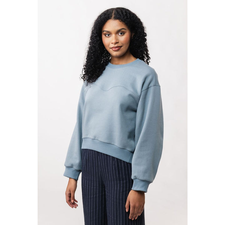 Woman wearing a light blue sweatshirt and dark pinstripe pants on a white background