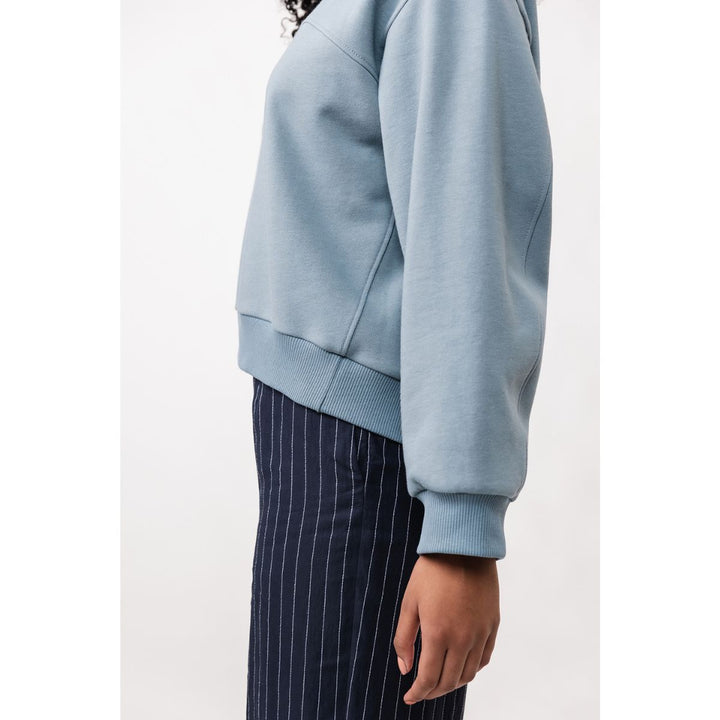 Person wearing a light blue sweatshirt and dark pinstripe pants on a white background