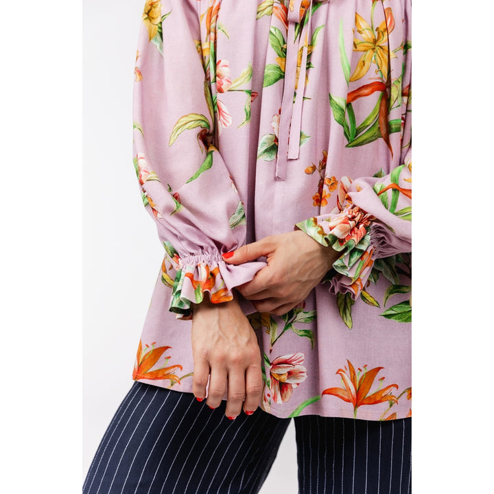 A close-up of a person wearing a light pink floral blouse with orange and green botanical print, gathered elastic cuffs, and dark navy pinstriped pants.
