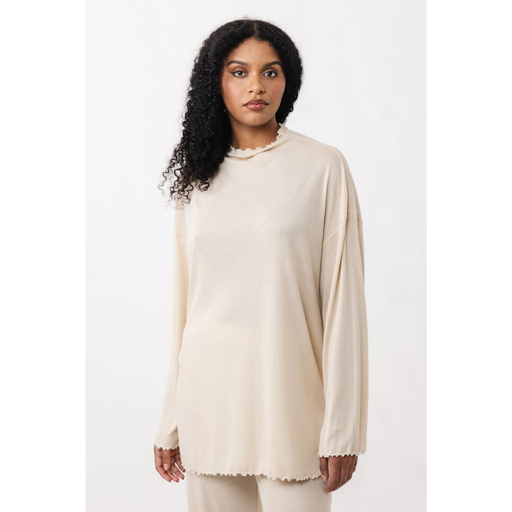 Woman wearing a beige long-sleeve top with lace trim on a white background