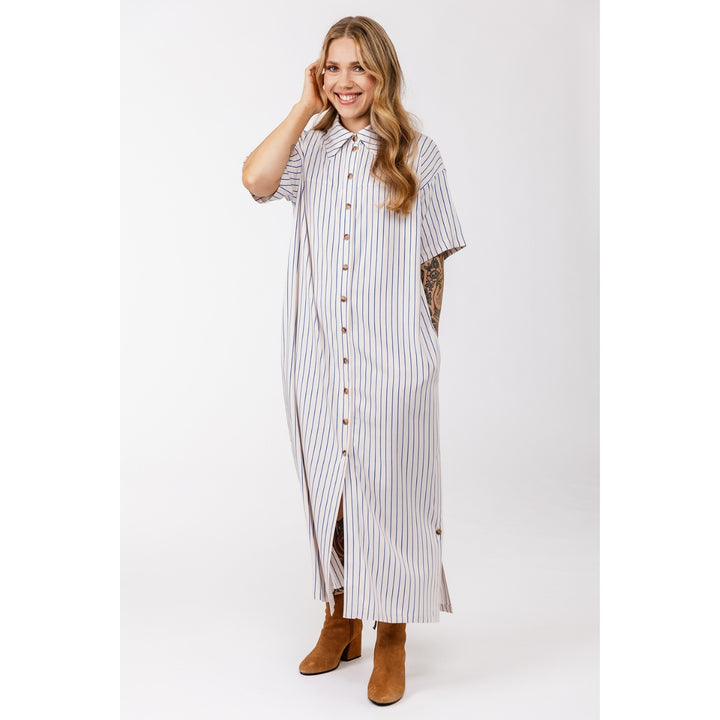 A woman modeling a long-sleeve, button-front maxi shirt dress with vertical blue and white stripes, styled with brown suede ankle boots against a light gray studio background.