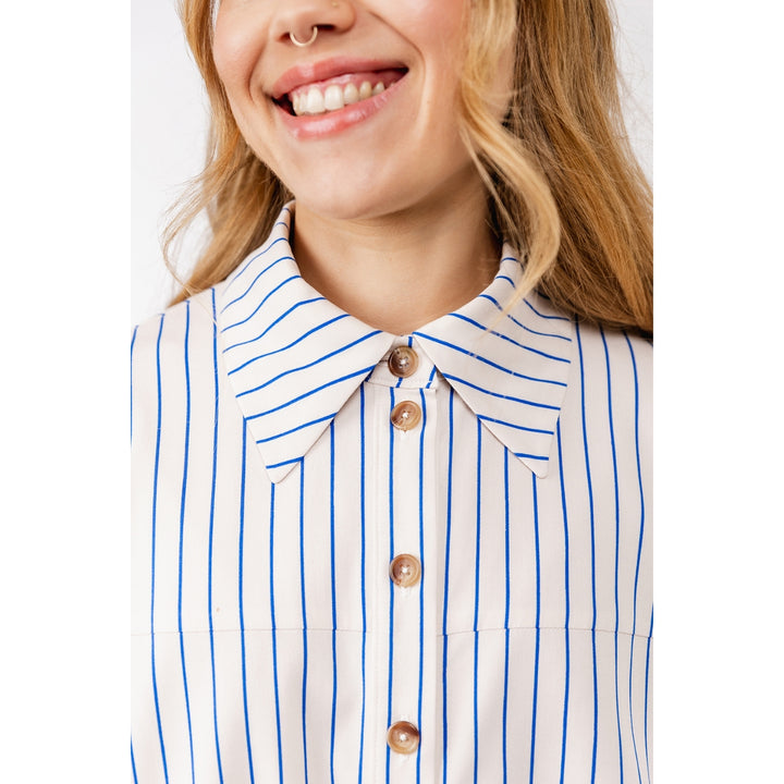 Close-up of a woman wearing a white collared button-front blouse with thin vertical blue stripes and brown buttons.