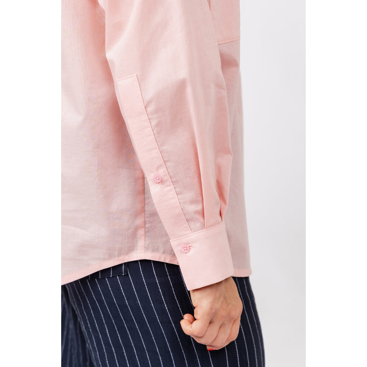 A close-up of a person wearing a light pink long-sleeve button-up shirt with dark navy pinstriped trousers, showing the sleeve cuff and hand.