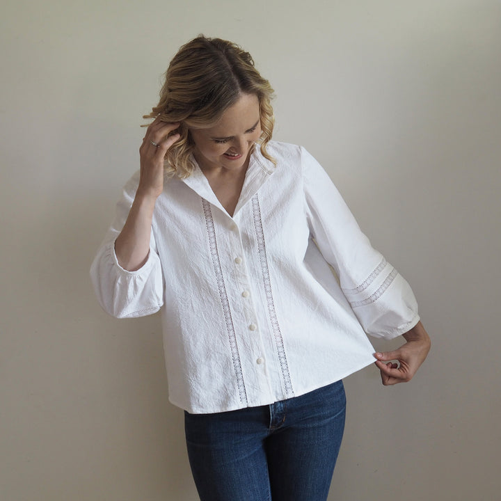 lady in the Nepheline blouse made in the white vintage textured cotton with lace inserts on the front and open collarless neckline.