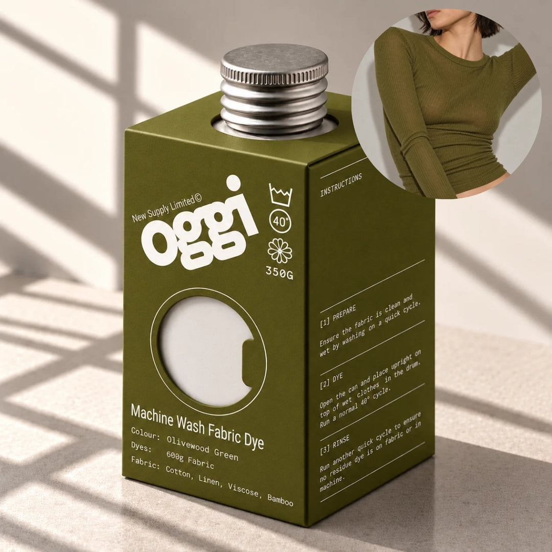 Oggi brand olive green machine wash fabric dye box with a silver metal cap, shown on a light surface with window shadow overlays. A circular inset shows a model wearing an olive green long-sleeve top.