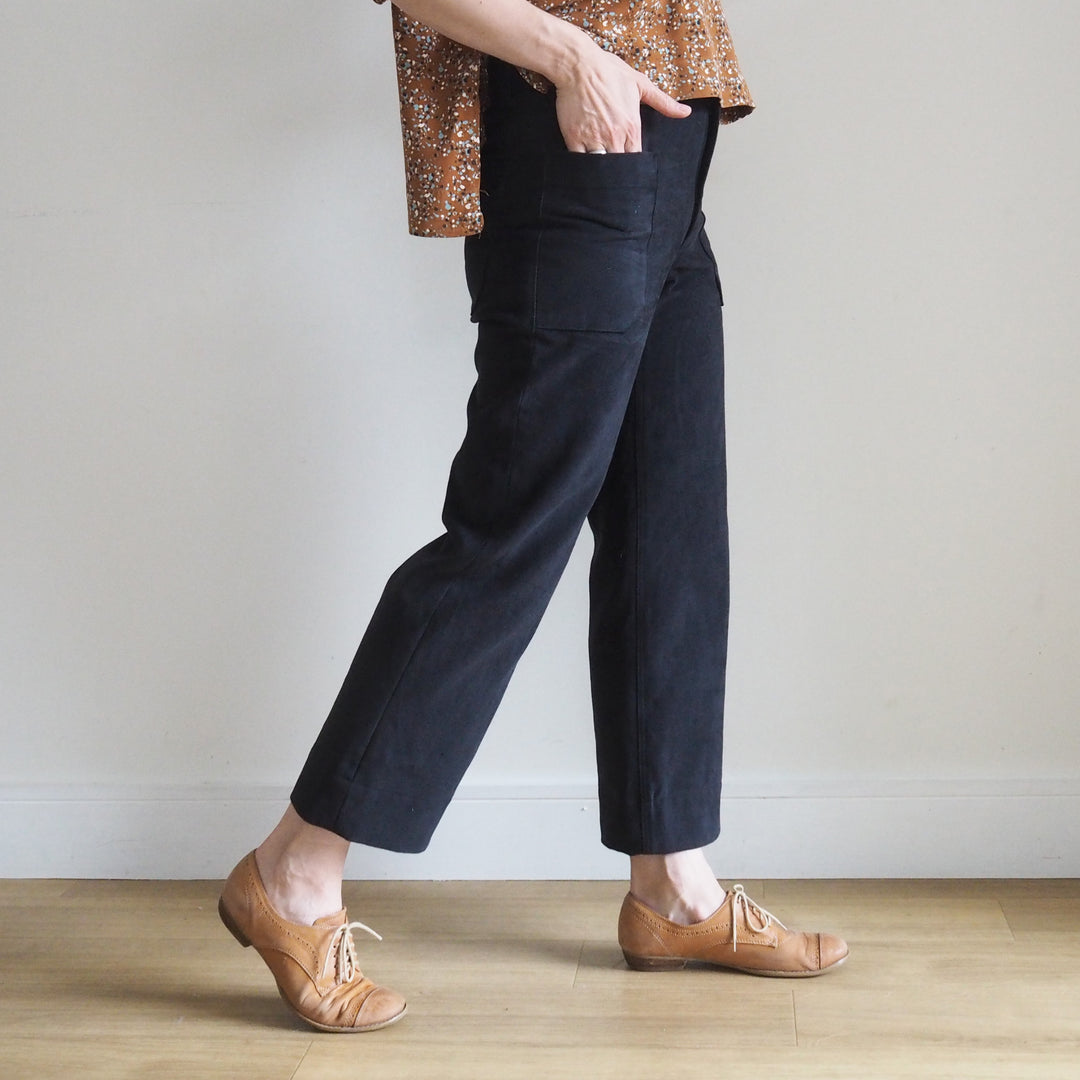 Model wearing the cropped version of the Oxbow trousers in black brushed denim with fitted waist and straight leg silhouette. View is from the side so you can see the front and back pockets
