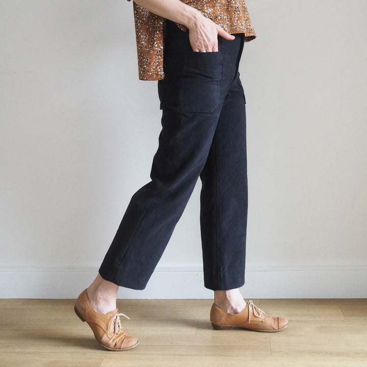 Model wearing the cropped version of the Oxbow trousers in black brushed denim with fitted waist and straight leg silhouette. View is from the side so you can see the front and back pockets