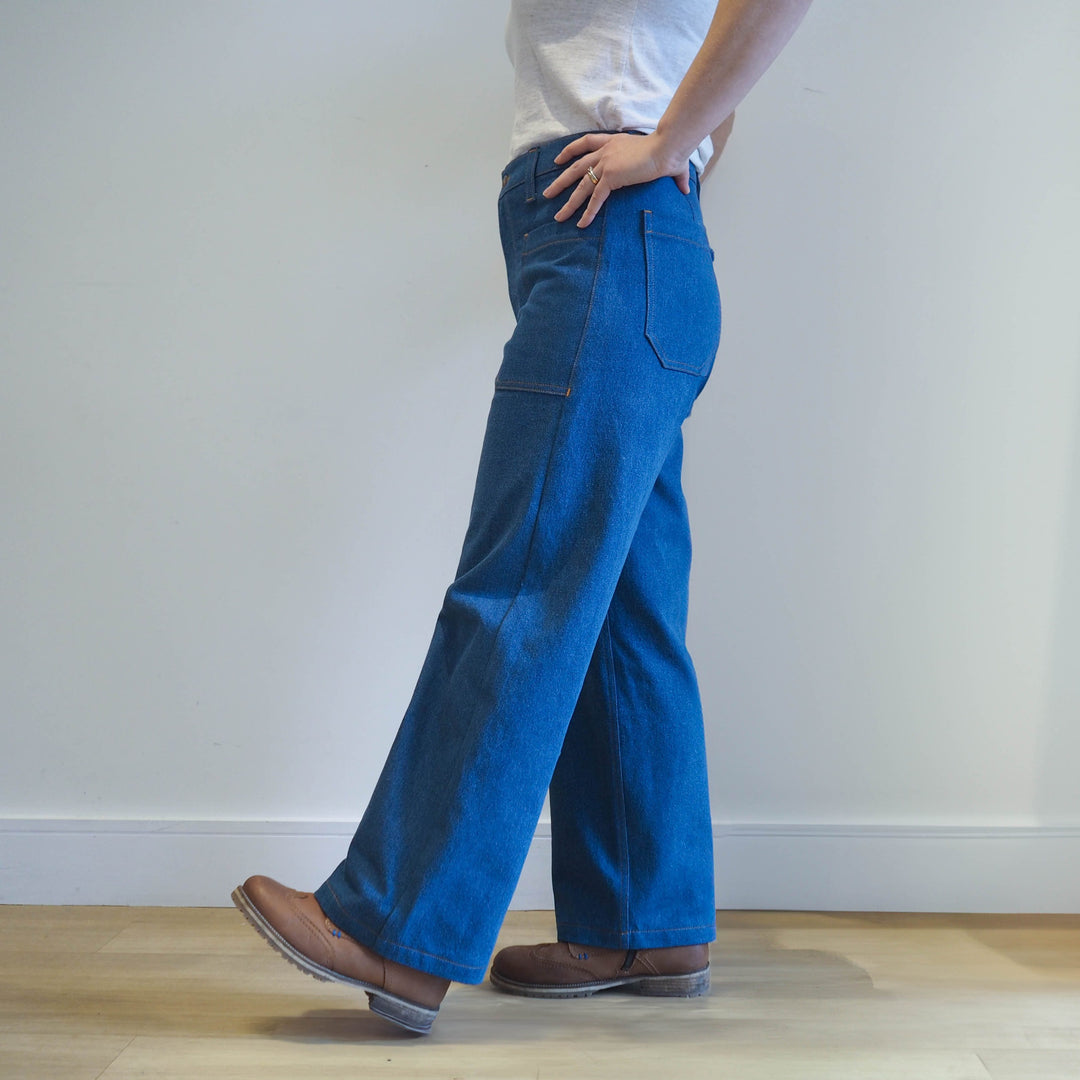 Model wearingf the Oxbow trousers in mid blue denim with fitted waist and straight leg silhouette. View is from the side so you can see the front and back pockets