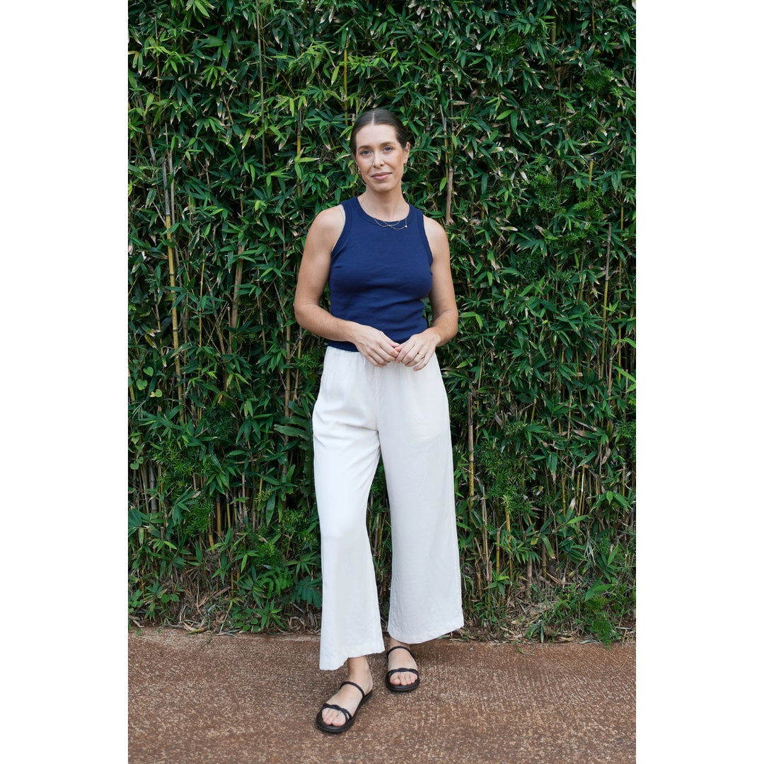 Woman in a blue top and white pants standing against a green bush