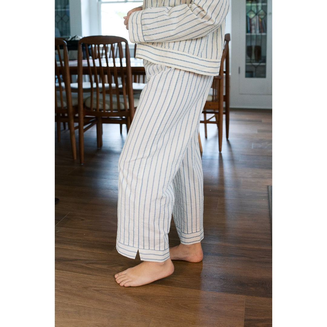 Person wearing striped pajama pants standing on a wooden floor in a room with chairs and a table.
