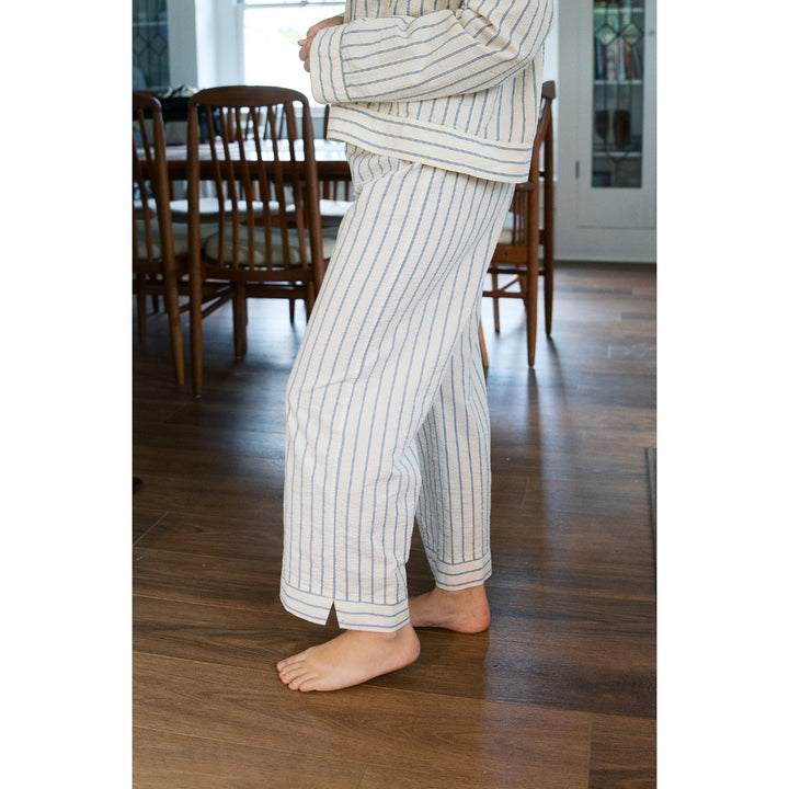 Person wearing striped pajama pants standing on a wooden floor in a room with chairs and a table.