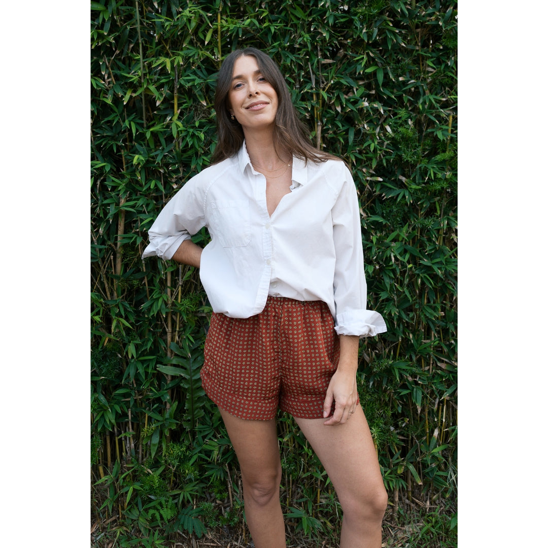 Woman wearing a white shirt and red checkered shorts standing against a green leafy background