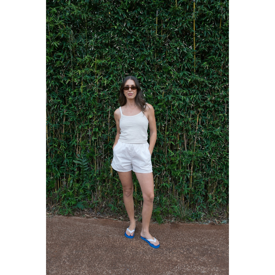 Woman in a white outfit standing against a green leafy background