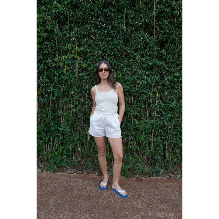 Woman in a white outfit standing against a green leafy background