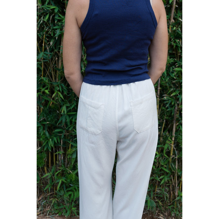 Person wearing a navy top and white pants standing against a green leafy background