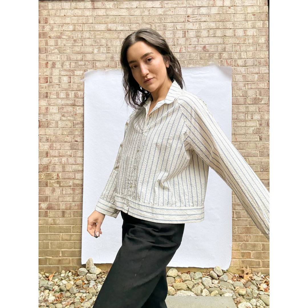 Woman wearing a striped shirt and black pants standing against a brick wall.