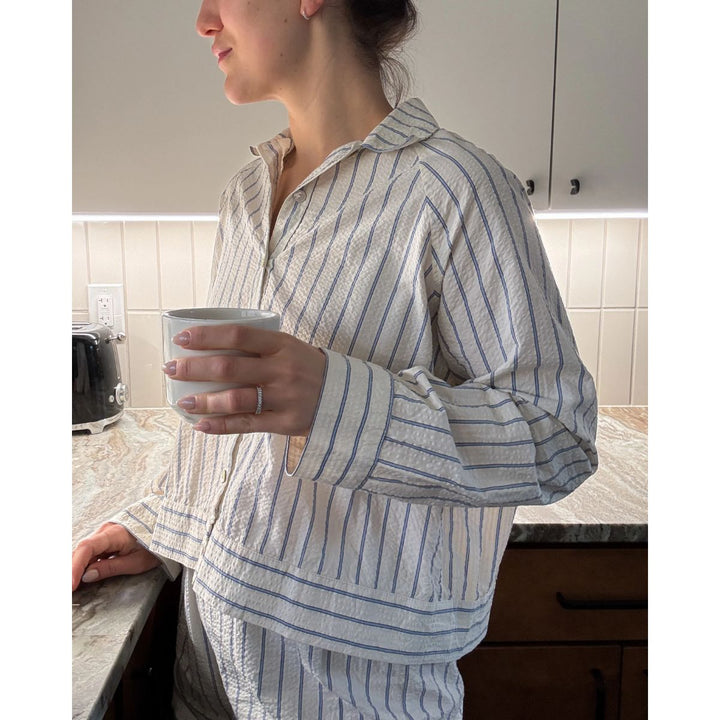 Person wearing a striped pajama set holding a mug in a kitchen.