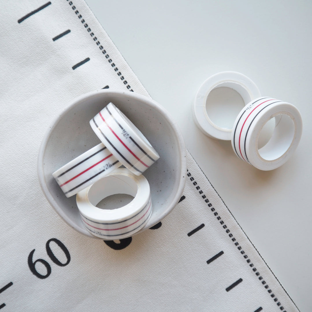 White tape with red and black stripes on a white surface with measurement markings.