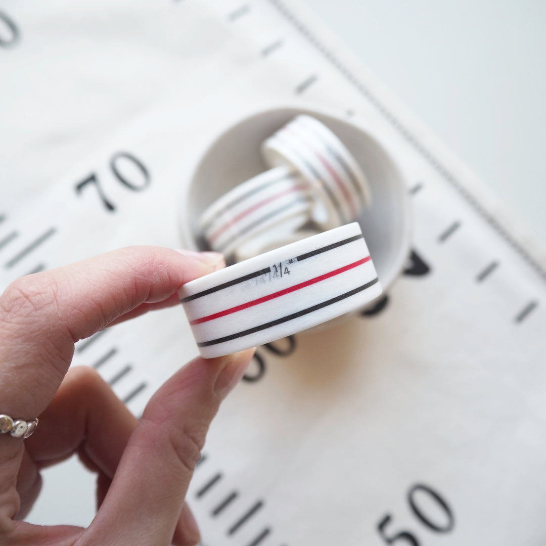 Hand holding a roll of washi tape with red and blue stripes against a blurred background
